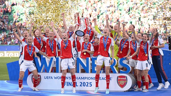 a group of celebrating women on a platform with a trophy, wearing Arsenal's red and white kits